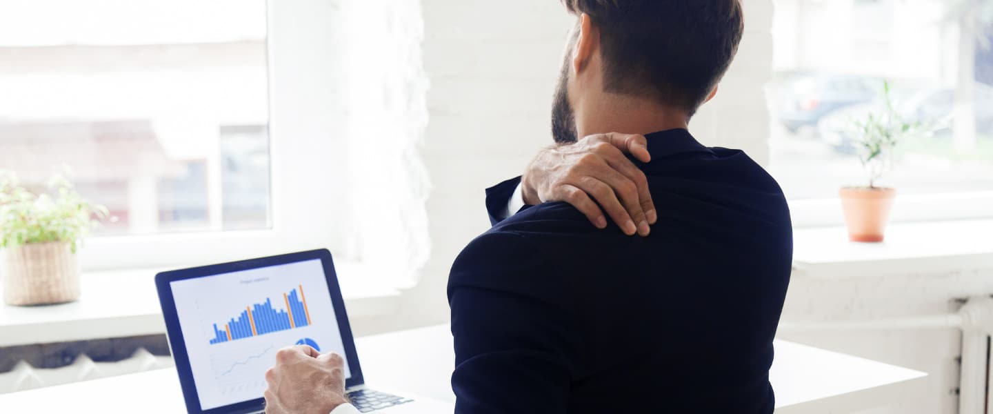 Mann sitzt am Laptop und fasst sich an den Rücken