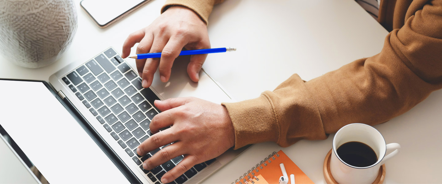 Person mit blauem Stift in der Hand benutzt einen Laptop