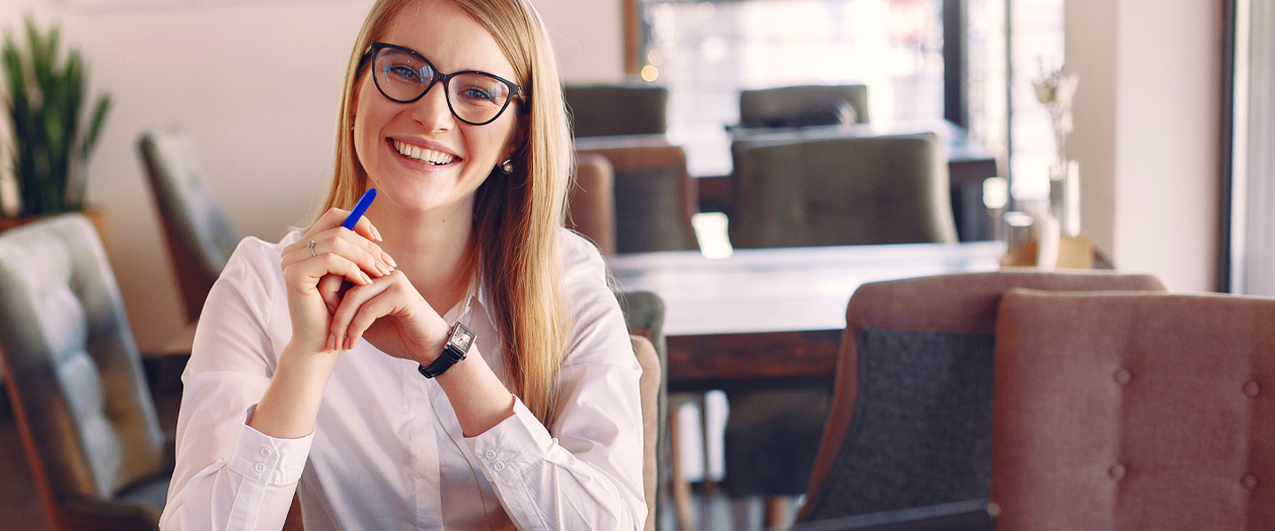 Frau mit Brille und Stift sitzt am Tisch und lacht